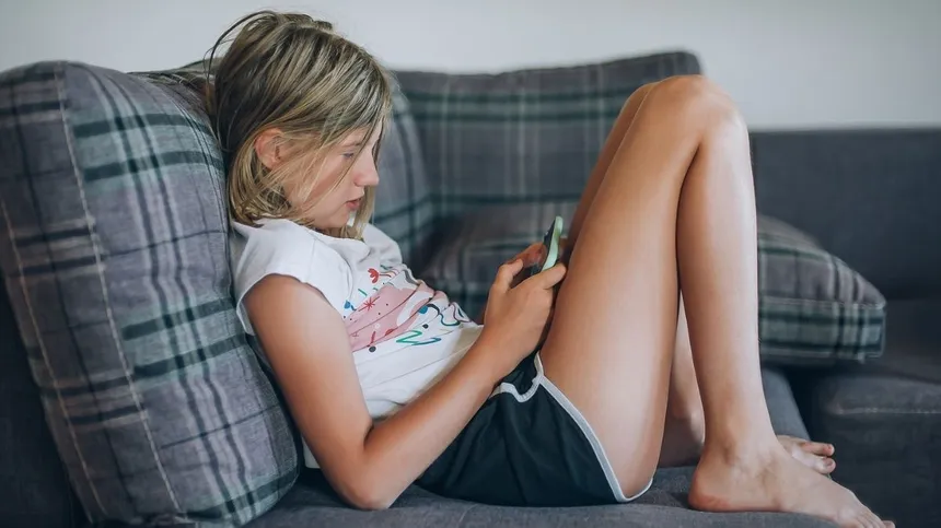 Mädchen sitzt auf dem Sofa und spielt am Smartphone: Gefahr von Cybergrooming