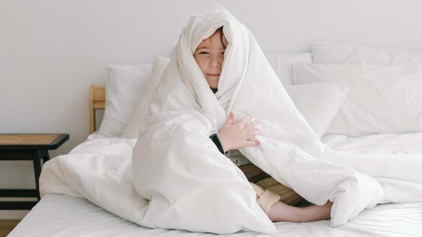 Kind in eine Decke gekuschelt im Bett