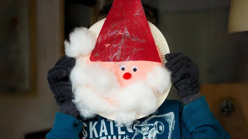 Kind hält gebastelten Weihnachtsmann aus Pappteller
