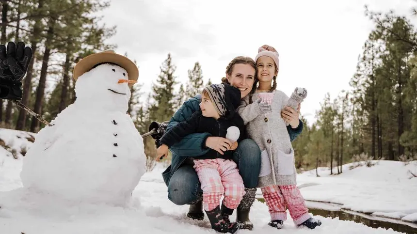 Mama baut mit ihren Kindern einen Schneemann
