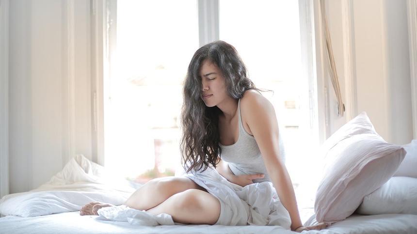 Unterleibsschmerzen ohne Periode: Frau sitzt mit Schmerzen auf einem Bett