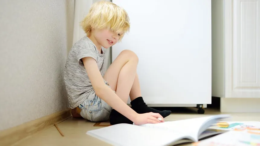 Kind sitzt mit einen Heft am Boden