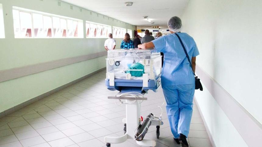 Eine Pflegerin schiebt ein Baby auf einer Pritsche entlang des Krankenhausflurs