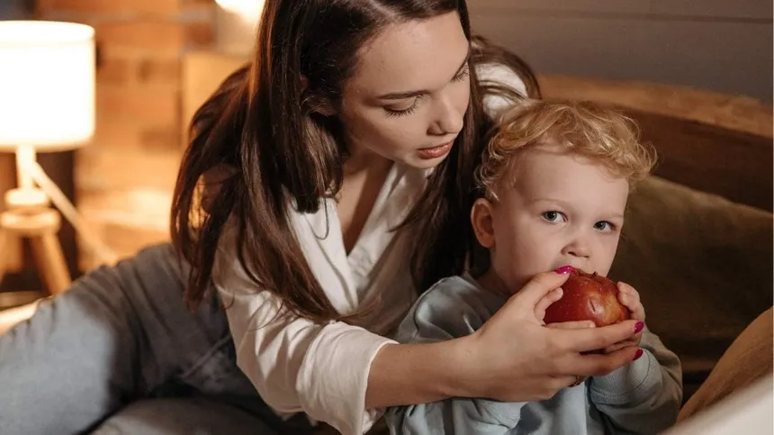 Kind isst Apfel und Mama hält ihn fest