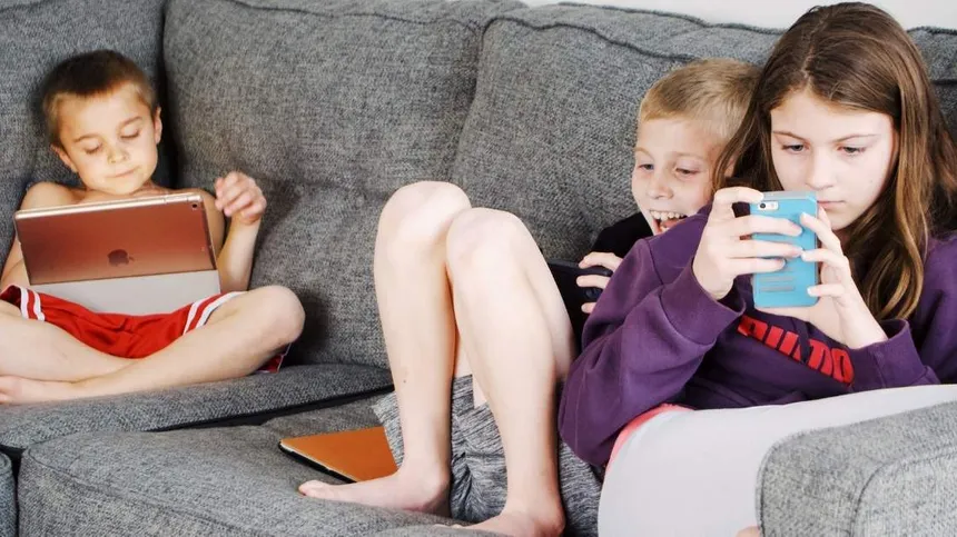 Kinder sitzen auf dem Sofa und spielen an Smartphone und Tablet