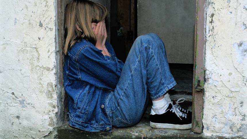 Ein Mädchen sitzt traurig auf einer Mauer