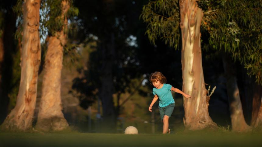 Kind spielt Fußball im Park unter Bäumen