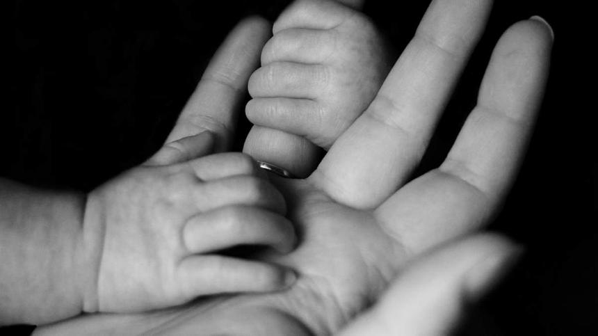Symbolbild: Hand einer Mutter mit zwei Babyhänden