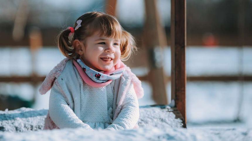 Symbolbild: Kind sitzt im Schnee und lacht